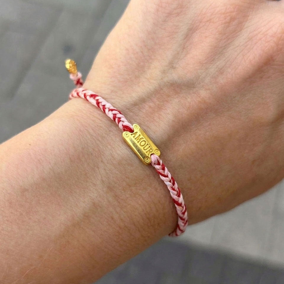 Red, pink, and white braided cord bracelet with an engraved gold "AMOUR" plaque