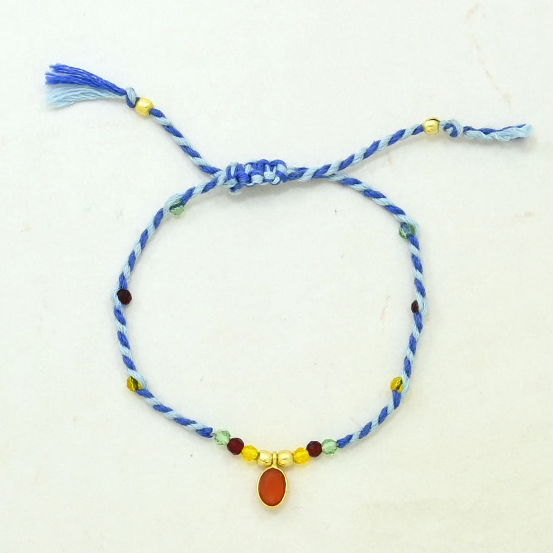 A blue braided cord bracelet with a sliding knot, decorated with small multicolored beads and a central oval amber stone.