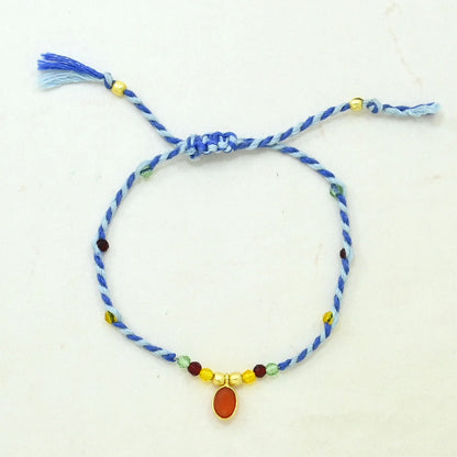 A blue braided cord bracelet with a sliding knot, decorated with small multicolored beads and a central oval amber stone.