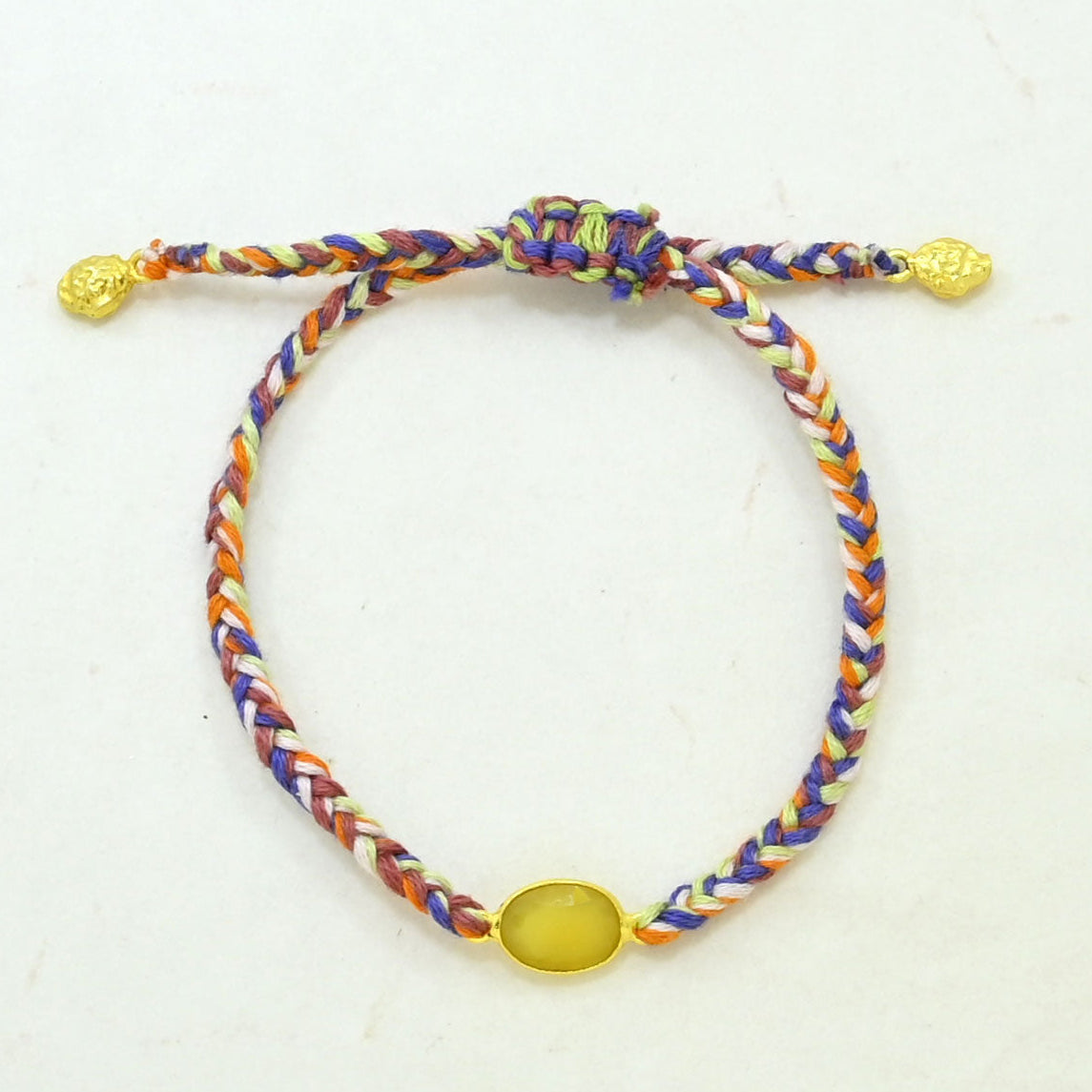 A multicolor braided cord bracelet with a knot closure, featuring textured gold-toned beads at the ends and a smooth oval yellow gemstone.