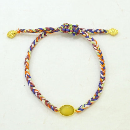 A multicolor braided cord bracelet with a knot closure, featuring textured gold-toned beads at the ends and a smooth oval yellow gemstone.