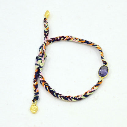 A multicolor braided cord bracelet with gold-toned metal accents, featuring a purple oval stone and a small gold charm.