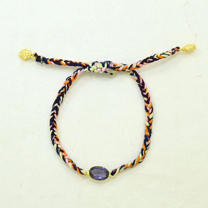 A braided adjustable cord bracelet with a purple oval gemstone set in gold at the bottom.