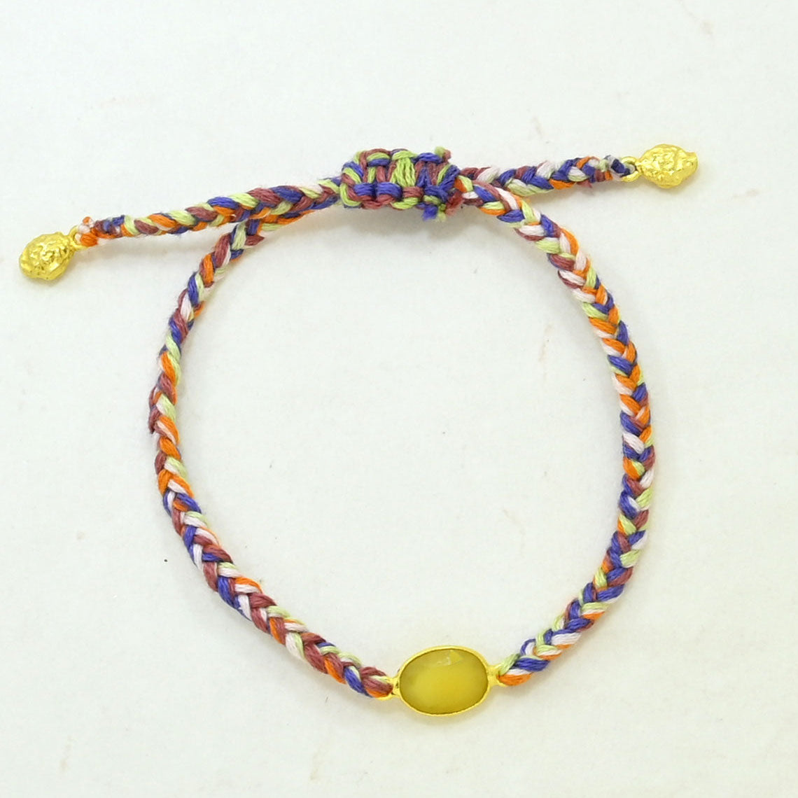 A multicolor hand woven cord bracelet with a yellow oval stone and gold-toned sliding knot ends