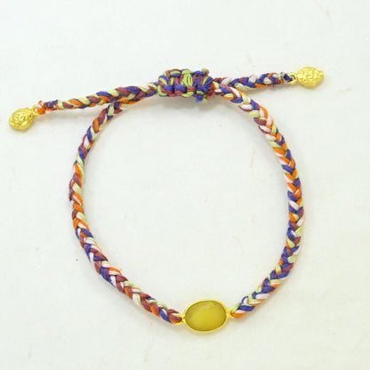 A multicolor hand woven cord bracelet with a yellow oval stone and gold-toned sliding knot ends
