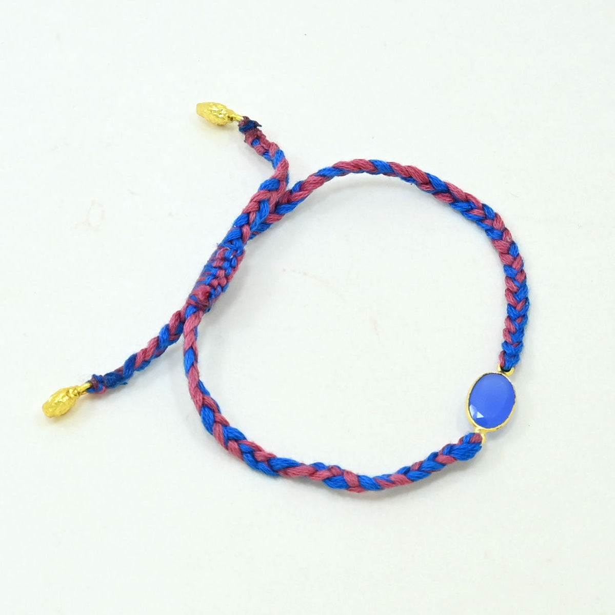 A braided cord bracelet in blue and red with a small oval blue stone and gold-tone metal accents-