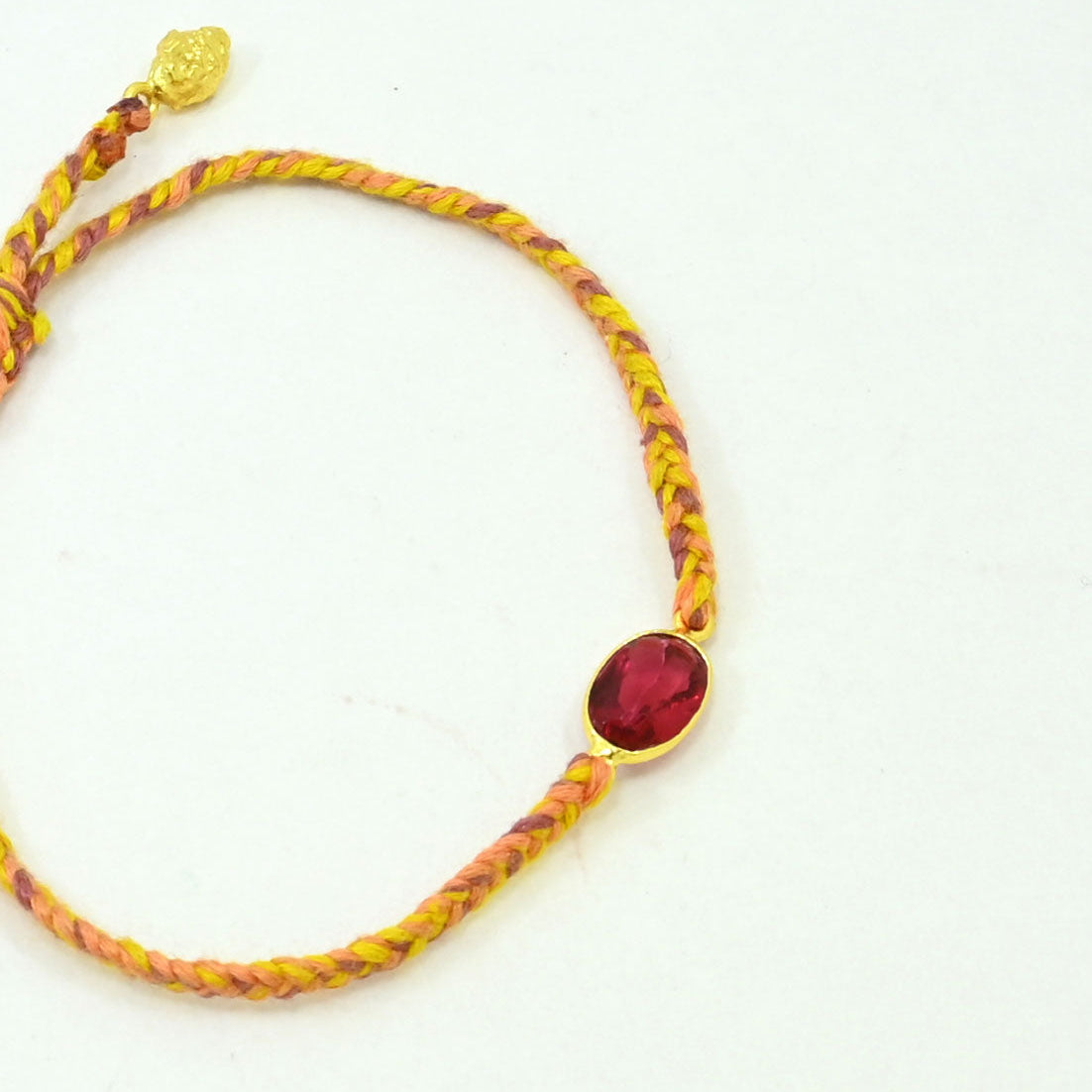 A braided yellow and orange cord bracelet with a central oval red gemstone in a gold bezel setting, shown on a plain white background.